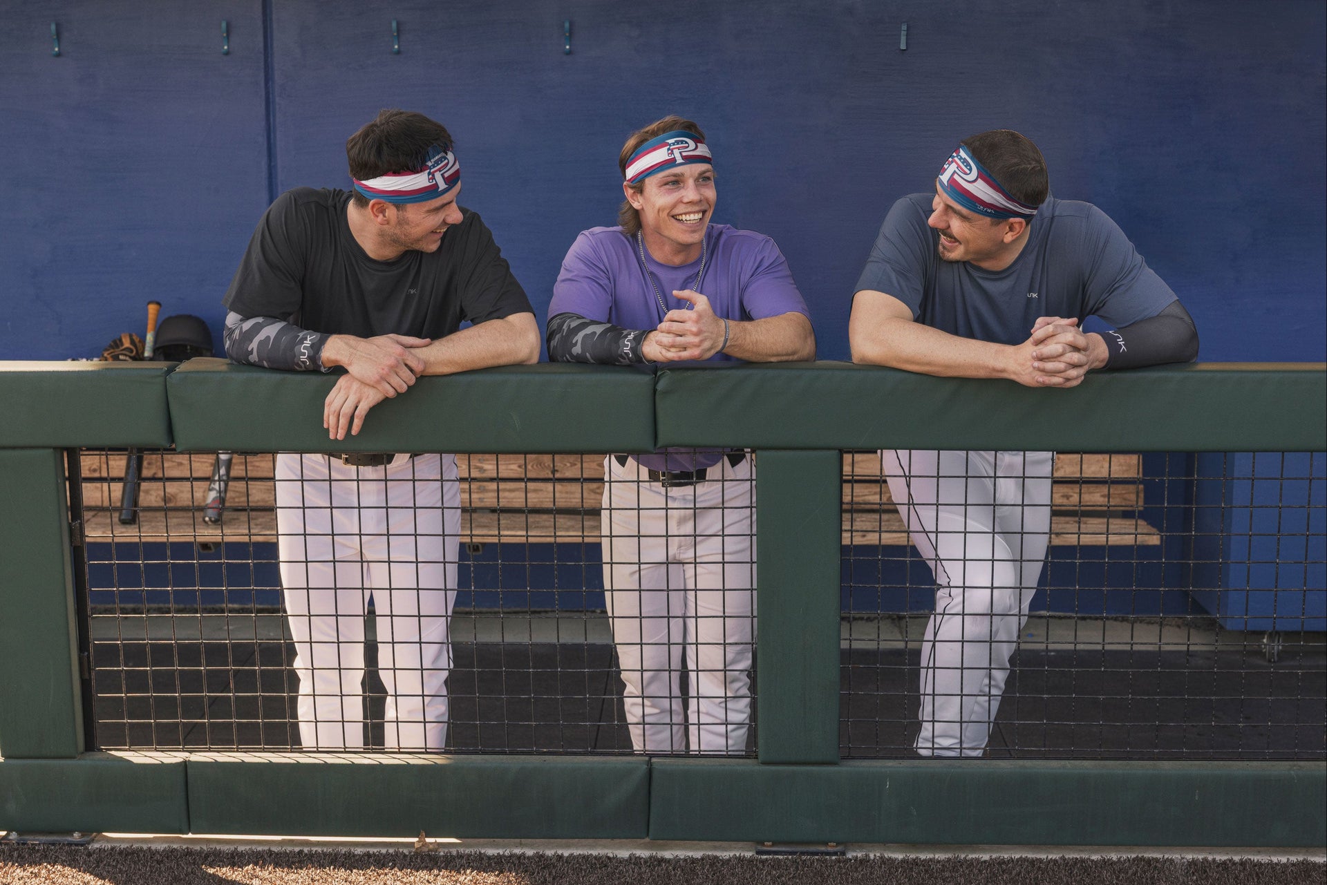 Three men wearing headbands leaning on a railing in a sports setting.